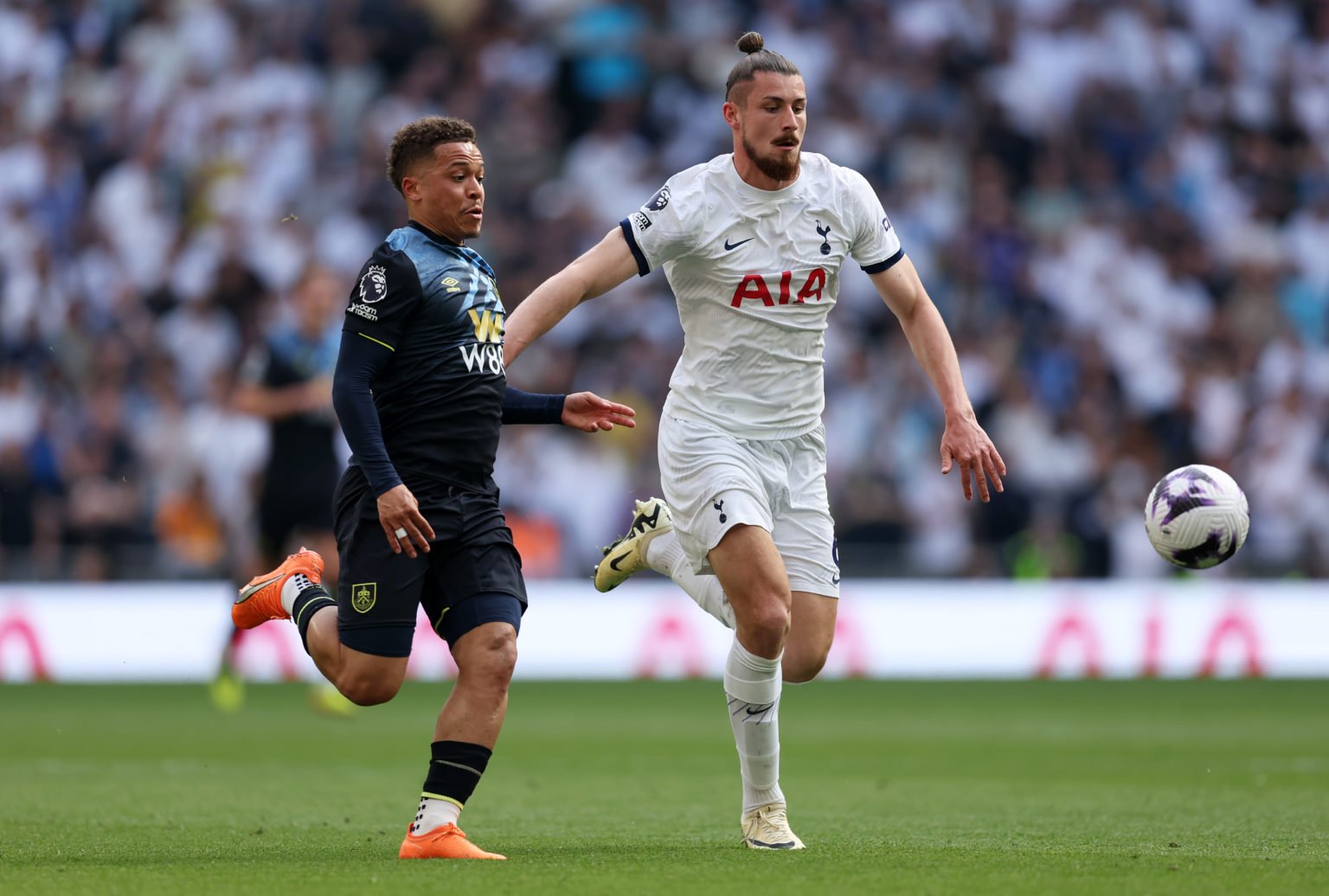 Radu Dragusin of Tottenham Hotspur runs with the ball under pressure from Vitinho of Burnley during the Premier League match between Tottenham Hots...